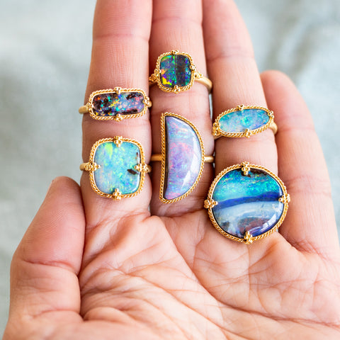 Five iridescent blue Boulder Opal rings set in 18k yellow gold, on a single hand.
