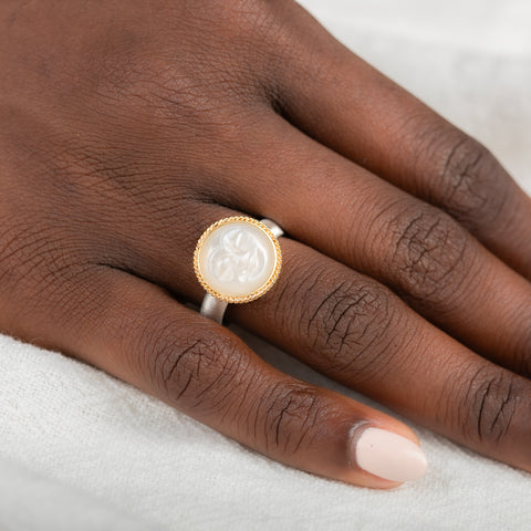 Close-up of a hand wearing a gold moonstone ring with a moon face on a white background