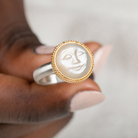 Gold moonstone ring with a moon face design held in a person's hand