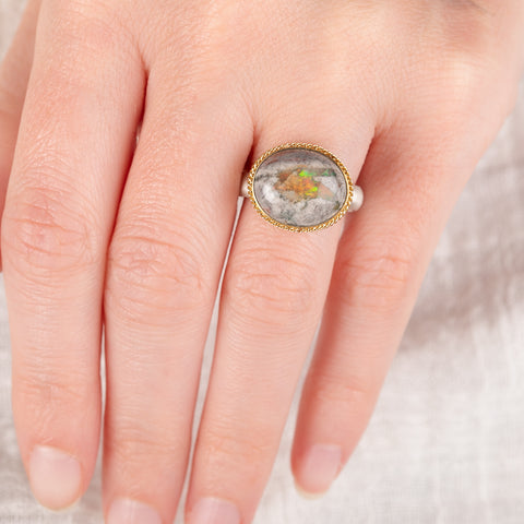Close up of a handmade ring on a finger with a mexican opal stone, gold setting and sterling silver band