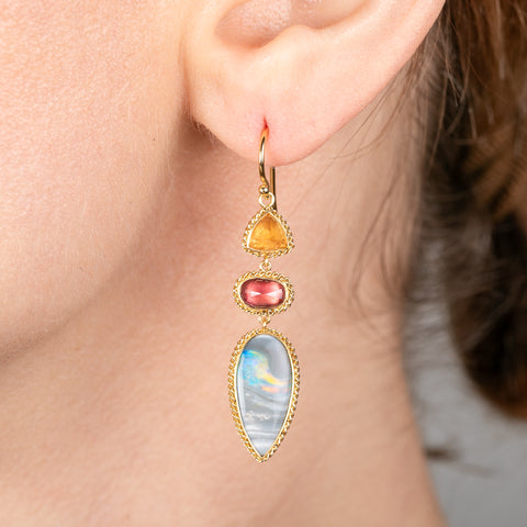 Close-up of a person wearing a colorful gemstone earring with gold frame.