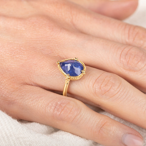 Gold ring with a teardrop-shaped tanzanite gemstone on a person's finger