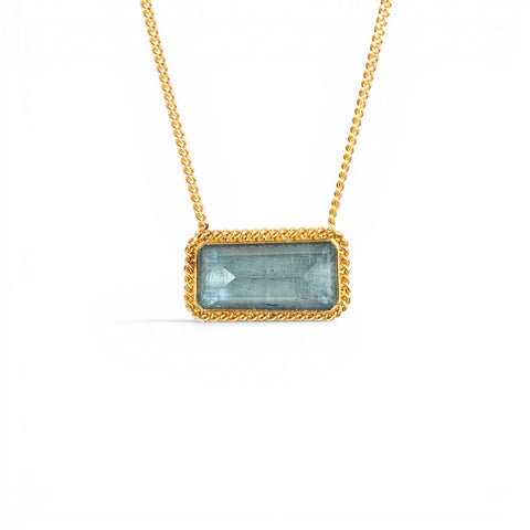 A gold chain necklace with a rectangular, light blue aquamarine gemstone pendant, framed by a textured gold bezel, shown against a plain white background.