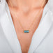 A gold chain necklace with a rectangular, aquamarine gemstone pendant, shown worn on a model's neck.