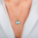 A gold necklace with a teardrop-shaped aquamarine gemstone pendant, shown worn on a model's neck.