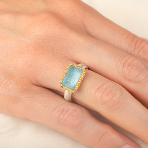 Handmade ring featuring an aquamarine gemstone set in an 18k gold bezel and paired with a sterling silver band, worn on a person's hand.
