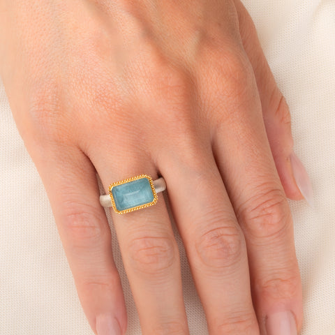 Handmade ring featuring an aquamarine gemstone set in an 18k gold bezel and paired with a sterling silver band, worn on a person's hand.