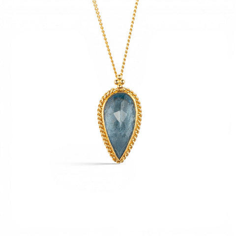 A gold necklace featuring an aquamarine gemstone, shown against a white backdorp.