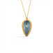 A gold necklace featuring an aquamarine gemstone, shown against a white backdorp.