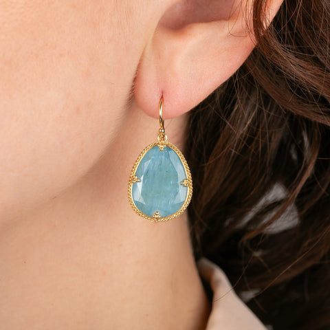 Gold earrings with aquamarine gemstones worn by a person