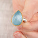 Close up of a hand holding an aquamarine ring with gold bezel and sterling silver band on white background