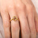Gold ring with a brown diamond on a person's finger against a neutral background