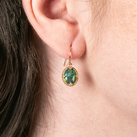 Gold earrings with green australian opal gemstones worn by a person