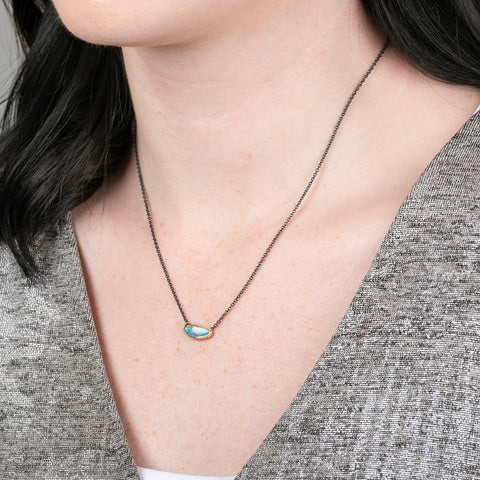 Australian opal gemstone necklace with a gold setting and oxidized silver chain on a person
