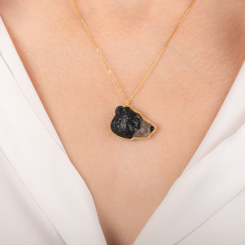 Gold necklace featuring a jasper gemstone carved into a black bear face worn on a model's neck.