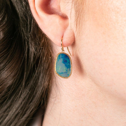Gold earrings with blue australian opal gemsotnes worn by a person