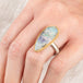 Close up of a person wearing a handmade fine jewelry boulder opal ring with an 18k gold bezel and sterling silver band