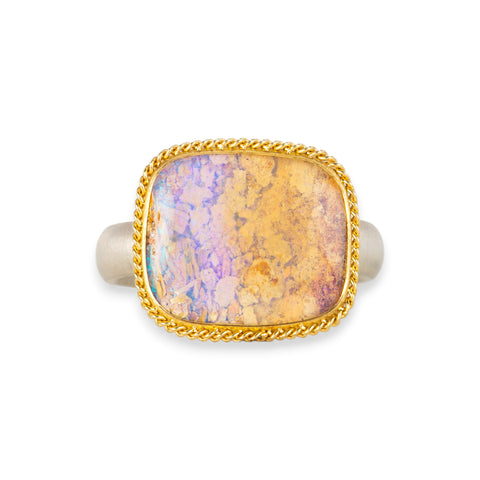 Handmade ring featuring a boulder opal gemstone set in an 18k gold bezel and paired with a sterling silver band, against a white background.
