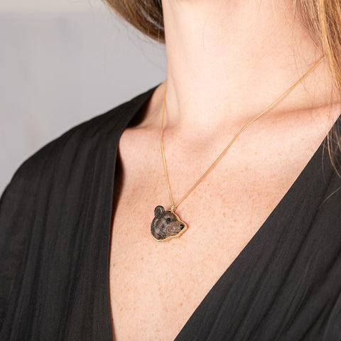 Handmade 18k gold necklace with a carved bear pendant worn by a person against a neutral background.