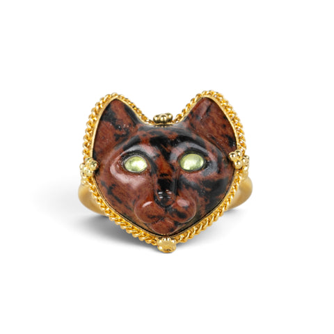 A gold ring featuring a carved dark brown and black cat face with green Tourmaline eyes, set against a clean white background.