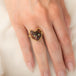 A gold ring featuring a carved dark brown and black cat face with green Tourmaline eyes, worn on a person's finger.