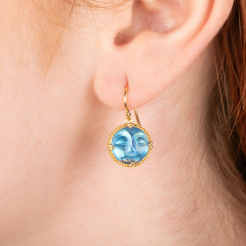 Gold earring featuring a moonstone carved as a moon face, worn in a person's ear.
