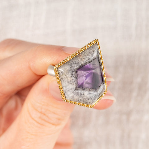 Close up of a person holding a handmade fine jewelry amethyst gemstone ring set in 18k gold with a sterling silver band