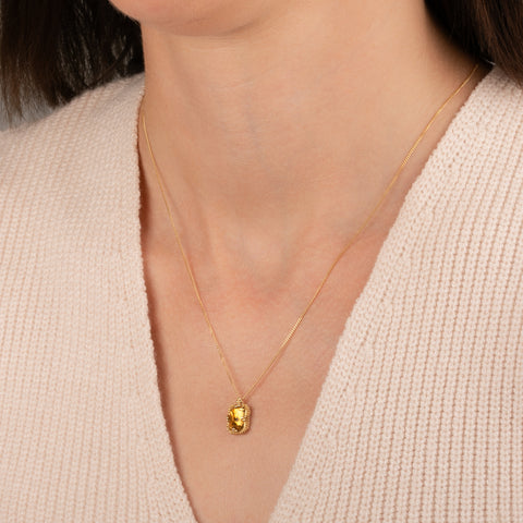 Gold necklace featuring a citrine gemstone worn on a person's neck.