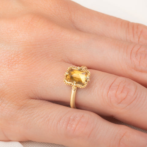 Gold ring featuring a citrine stone set in an 18k gold bezel, worn on a person's finger.