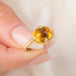 A gold ring featuring a citrine gemstone, held in a hand.