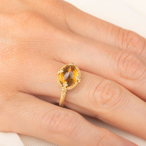 A gold ring featuring a citrine gemstone, worn on a finger.