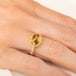 A gold ring featuring a citrine gemstone, worn on a finger.