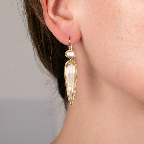 A model wears a handmade 18k gold earring featuring crystal quartz and rutilated quartz gemstones.