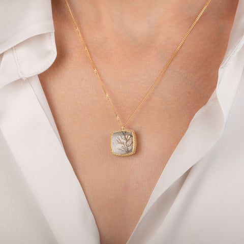 Gold necklace featuring a dendritic stone worn on a model's neck.