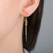 Close up of a gold tassel earring featuring a row of four champagne diamonds, worn in a person's ear.