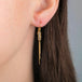 Gold earrings with gold tassels dangling between rows of four silver diamonds, shown in a person's ear.