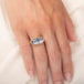 An oval ring featuring a textured light blue dumortierite stone in a yellow gold bezel setting and a matching gold band, worn on a person's finger.