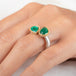 A gold and silver ring featuring two emerald stones worn on a person's finger