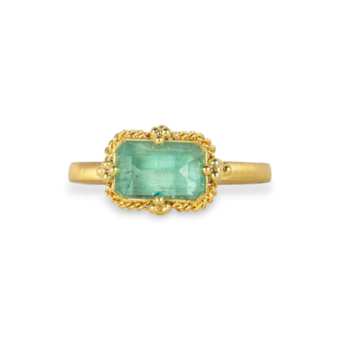 A gold ring featuring a light green emerald gemstone, against a white background.