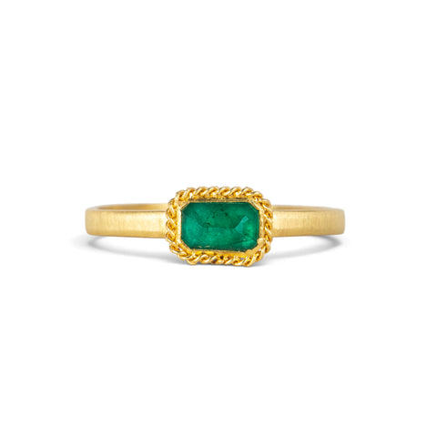 A yellow gold ring featuring a rectangular emerald gemstone in an 18k gold bezel setting, shown on a clean white background.