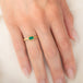 A yellow gold ring featuring a rectangular emerald gemstone in an 18k gold bezel setting, worn on a person's finger.