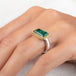 A rectangular emerald stone ring with a gold bezel and a sterling silver band, worn on a finger