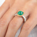 A ring featuring a cushion-cut emerald gemstone in a gold bezel setting, paired with a silver band, worn on a hand
