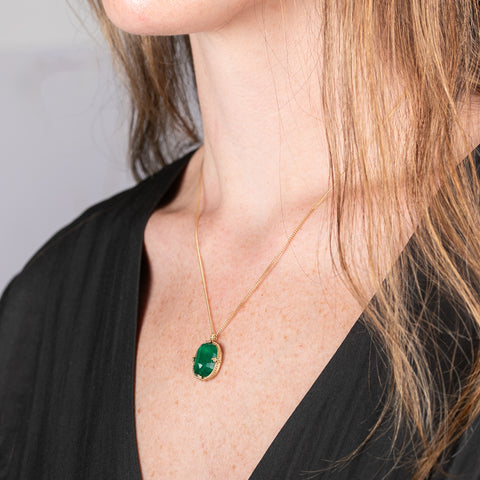Close-up of a model wearing a handmade, one-of-a-kind gold necklace with an emerald pendant.