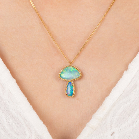Boulder opal pendant necklace in mushroom design on a gold chain against a person in a white top