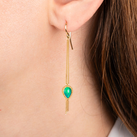 Gold drop earrings with teardrop-shaped opal gemstones and dangling chain accents, shown on a person's ear