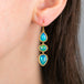 Gold earrings featuring a trio of iridescent Ethiopian opal gemstones, worn on a model's ear.