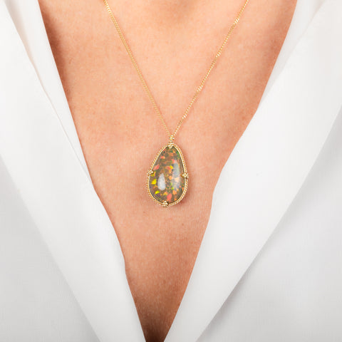 A teardrop-shaped Ethiopian Opal necklace set in a gold bezel worn on a person's neck