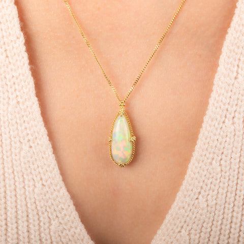 Gold necklace featuring an Ethiopian opal gemstone set in a handcrafted 18k gold bezel and strung from a matching gold chain, worn on a person's neck.