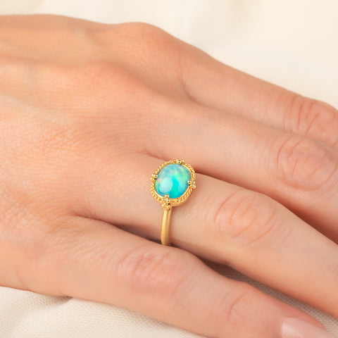 Gold ring featuring a vibrant Ethiopian opal stone, worn on a person's finger.